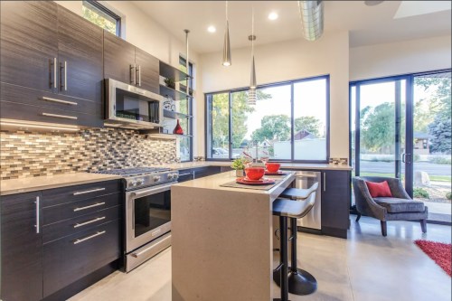 Modern kitchen with dark cabinetry, stainless steel appliances, a central island, and large windows letting in natural light.