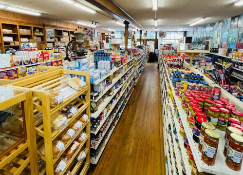 A wide aisle in a grocery store filled with shelves of various food products and jars, with wooden accents and bright lighting.