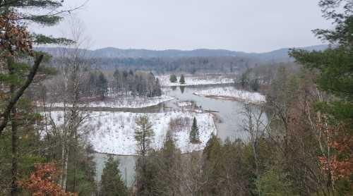 A serene winter landscape featuring a winding river surrounded by snow-covered trees and distant mountains.