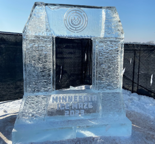 An ice structure with "Minnesota Ice Maze 2023" carved into it, set against a clear blue sky.