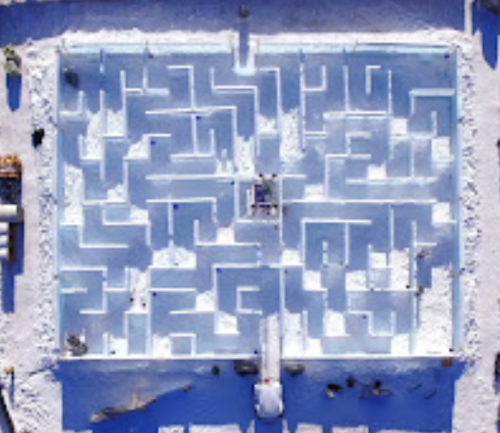 Aerial view of a snow maze with intricate pathways and walls, surrounded by a snowy landscape.