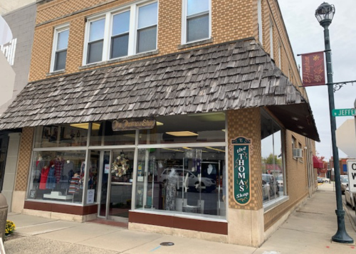 A storefront with a shingled roof, featuring large windows displaying clothing and decor, located on a city street.