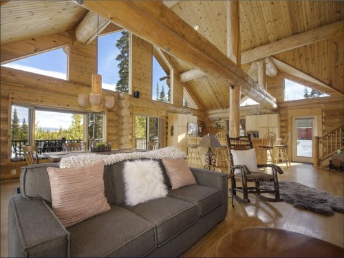 Cozy log cabin interior with wooden beams, large windows, and a comfortable sofa, featuring a warm, inviting atmosphere.