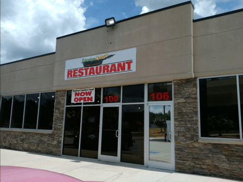 Exterior of a restaurant with a large sign reading "RESTAURANT" and a "NOW OPEN" banner on the door.