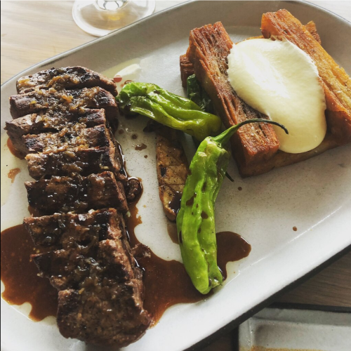 A plate featuring sliced steak, roasted green peppers, and crispy yucca topped with creamy sauce.