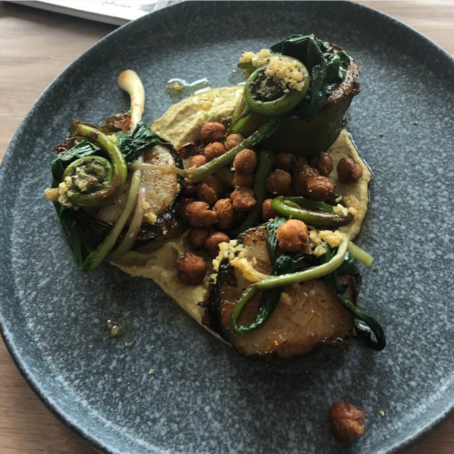 A plate featuring grilled vegetables, chickpeas, and a creamy sauce, garnished with herbs on a textured blue dish.