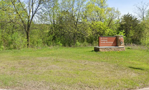 Sign for St. Croix National Scenic Riverway, surrounded by green grass and trees on a sunny day.