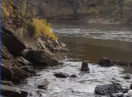 A serene river scene with rocky banks and autumn foliage along the water's edge.