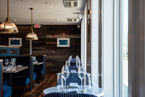 Interior of a modern restaurant featuring blue booths, wooden walls, and elegant table settings with glassware.