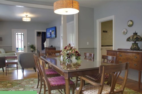 A cozy dining area with a wooden table, floral centerpiece, and a view of a living room with a TV and decorative lamp.