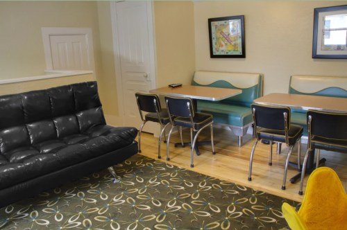 A cozy dining area with a black sofa, green and beige tables, and black chairs on a patterned rug.