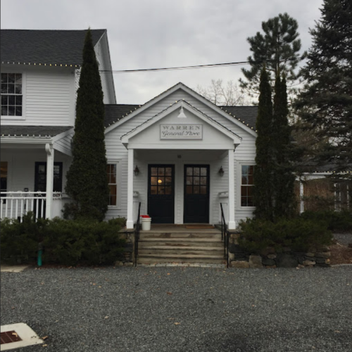 A white building with a sign reading "Warren General Store," surrounded by trees and gravel.