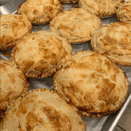 A tray of freshly baked golden-brown pies with flaky crusts, arranged in a neat row.