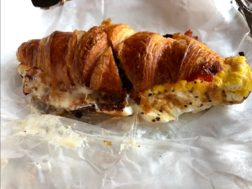 A croissant filled with melted cheese and a fried egg, resting on crumpled parchment paper.
