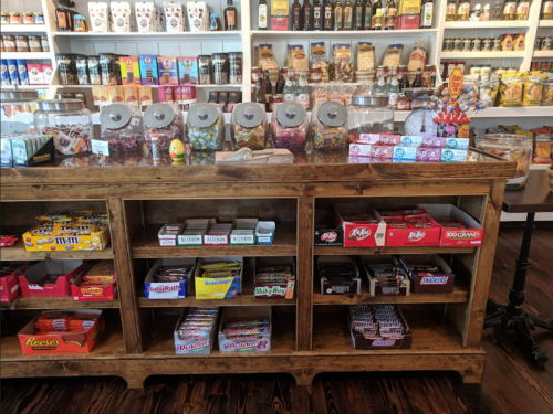 A wooden display filled with various candies and snacks, with jars of sweets and colorful packaging on shelves behind.