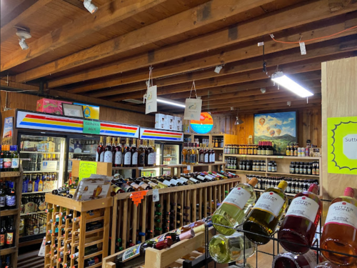 A cozy store interior with wooden beams, shelves of wine, and colorful signage displaying various beverages.