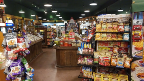A cozy store aisle filled with various snacks and packaged goods on shelves, with a wooden counter in the background.