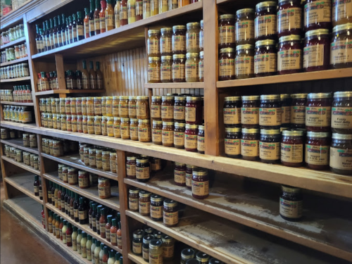 A wooden shelf filled with jars of various sauces and condiments, neatly organized in rows.