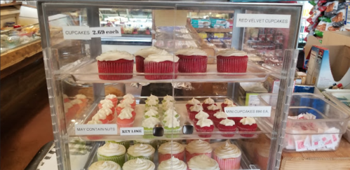 Display case filled with various cupcakes, including red velvet and mini cupcakes, with price labels visible.