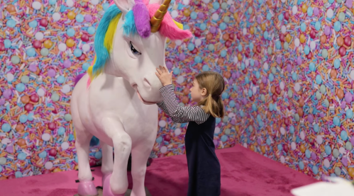 A child interacts with a colorful unicorn statue in a vibrant, candy-themed room.