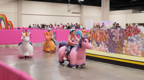 Children ride colorful unicorn-themed toy vehicles in a vibrant, pink-themed indoor space.