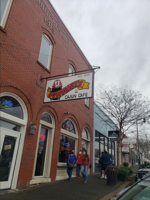 Sign for "Gumbo's a Cajun Cafe" on a brick building, with people walking by on a cloudy day.