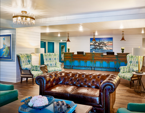 A stylish hotel lobby featuring a brown leather sofa, green patterned chairs, and a wooden reception desk.