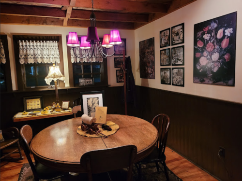 Cozy dining area with a round wooden table, purple lamps, floral artwork, and warm lighting.