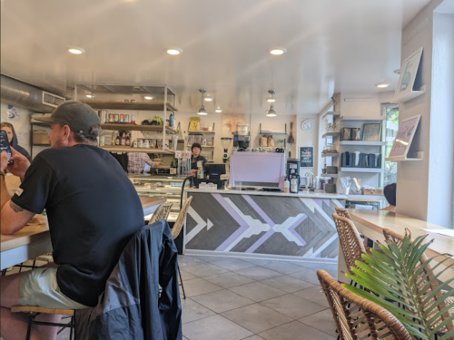 A cozy café interior with a counter, barista, and a customer sitting at a table. Bright and inviting atmosphere.