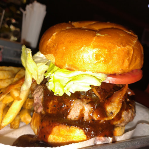 A close-up of a juicy burger with lettuce, tomato, and bacon, served with a side of crispy fries.