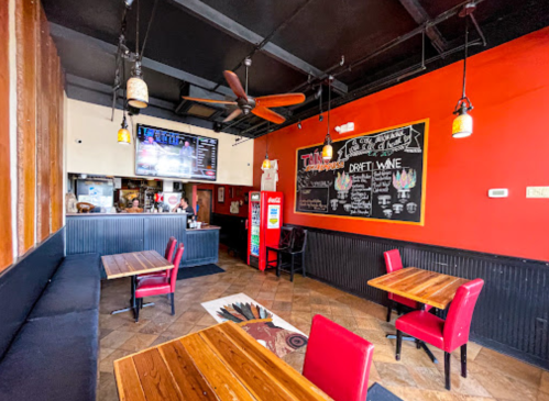 Interior of a cozy restaurant featuring wooden tables, red chairs, a chalkboard menu, and a soda machine.