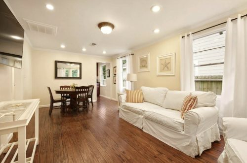 Cozy living area with a white sofa, dining table, and warm wooden floors, featuring soft lighting and decorative art.