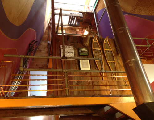 Interior view of a staircase with wooden walls, ski equipment, and a mounted deer head, featuring colorful accents.