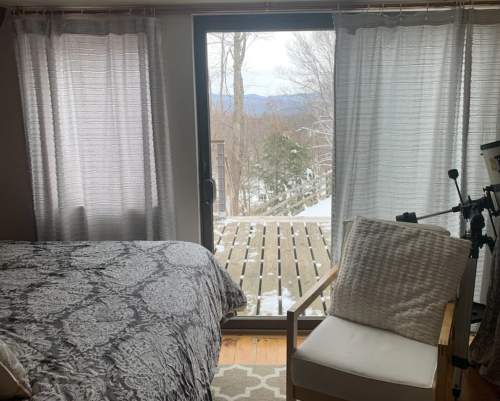 Cozy bedroom with a patterned bedspread, a chair, and large windows overlooking a snowy landscape.