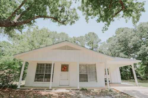 A white house with a front porch, surrounded by green trees and a clear blue sky.