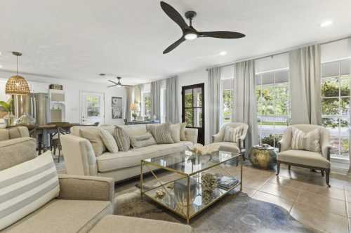 Bright living room with modern furniture, a glass coffee table, and large windows, featuring neutral tones and stylish decor.