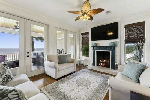 Cozy living room with a fireplace, large windows, and a view of the ocean, featuring light-colored furniture and decor.