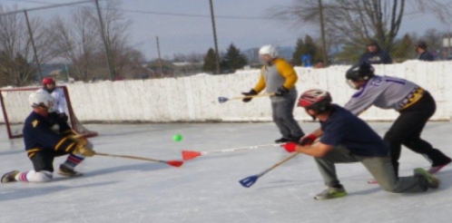 A group of players competes in a game of broomball on an outdoor ice rink.