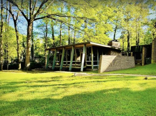 A modern house with large windows, surrounded by lush green trees and grass, set in a tranquil outdoor environment.