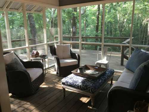 Cozy screened porch with wicker furniture, a coffee table, and a view of a wooded area outside.