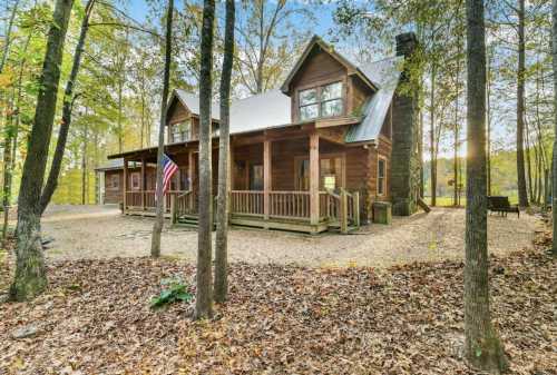 A rustic wooden cabin surrounded by trees, featuring a porch and an American flag, set in a serene natural landscape.