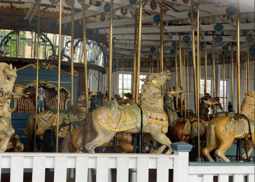 A vintage carousel with ornate, painted horses and golden poles, set in a bright, open space.