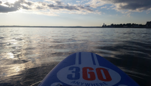 View from a paddleboard on calm water, with a distant shoreline and cloudy sky in the background.