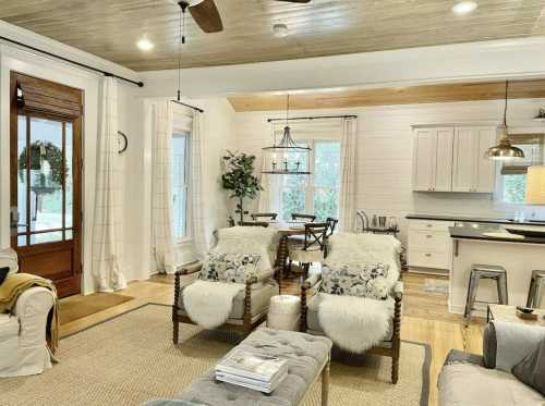 Cozy living room with two armchairs, a dining area, and a kitchen, featuring light colors and natural wood accents.