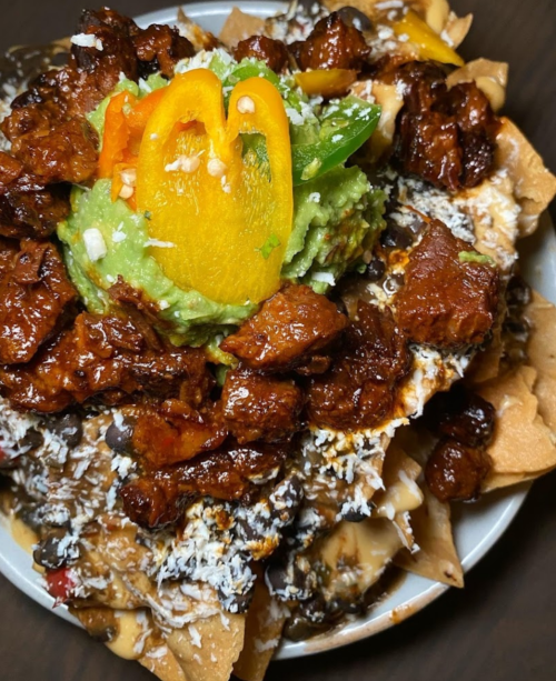 A bowl of nachos topped with guacamole, peppers, black beans, and seasoned meat, drizzled with cheese.