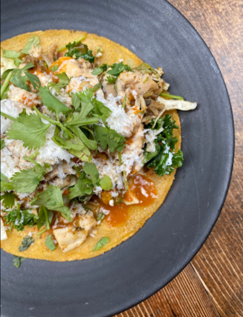 A close-up of a taco topped with shredded chicken, cilantro, cheese, and sauce on a black plate.