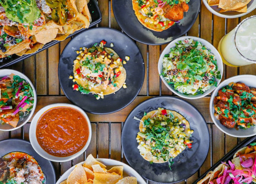 A vibrant spread of tacos, nachos, and bowls with fresh toppings, served on wooden tables.