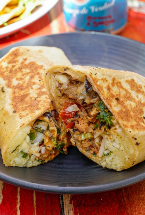 A close-up of a halved burrito filled with rice, beans, and vegetables on a dark plate.