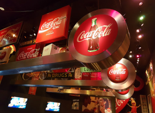 Interior of a vibrant Coca-Cola themed space with large circular signs and retro advertisements on the walls.