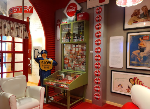 A colorful Coca-Cola exhibit featuring vintage memorabilia, a "Slow School Zone" sign, and retro decor.